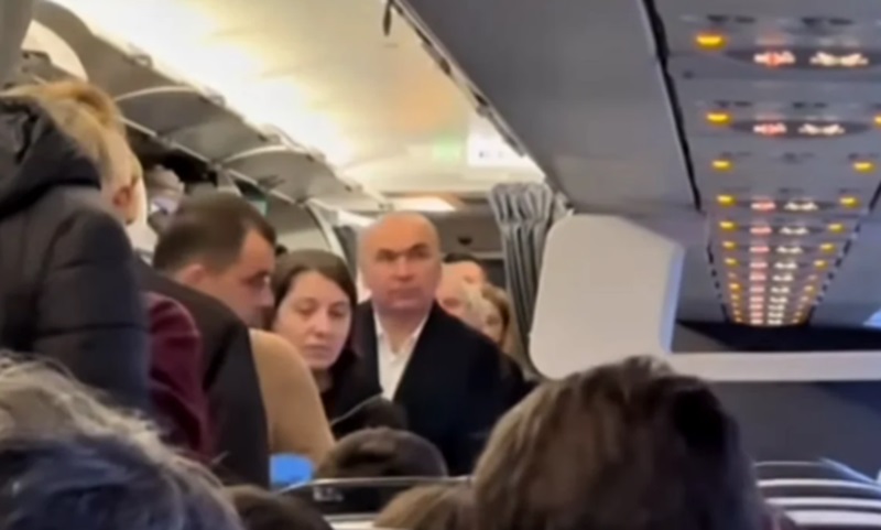 Summitul de la Londra. Ilie Bolojan, filmat într-un avion de linie, la clasa economic – preşedintele interimar a ajutat un alt pasager să-şi aşeze valiza