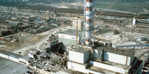 Industrial ruin: shattered buildings and scattered debris around a damaged power plant site with a tall striped lattice tower in the foreground.