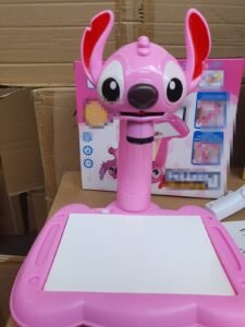 Pink kids' drawing tablet with a wide-eyed cartoon dog head on top and a white drawing surface behind it, set on a cardboard backdrop.