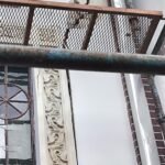 Cracked plaster on an exterior wall behind rusty scaffolding during renovation for a building.