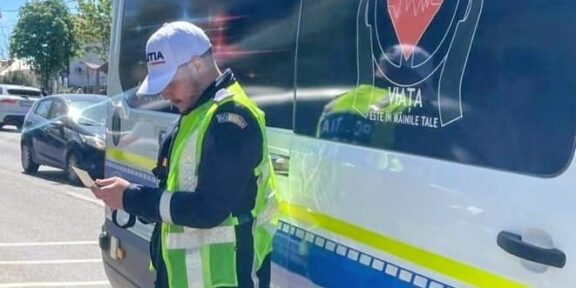 Policeman in a bright vest stands beside a blue-and-white police van, looking at a handheld device.