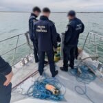Border police officers on a boat by the water, examining nets and blue ropes on deck.