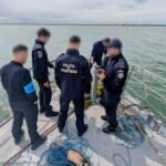 Border police officers on a boat examining objects from the water, with tangled ropes and nets on deck. (informative scene)
