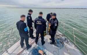 Border police officers on a boat examining objects from the water, with tangled ropes and nets on deck. (informative scene)