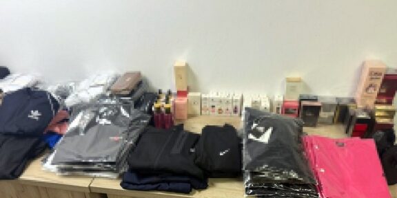 Stacks of folded jackets and clothing on a wooden table, with boxes and small items in the background.
