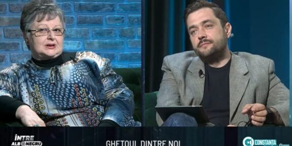 Split-screen interview on a TV talk show: an older woman in a patterned blouse on the left and a man in a gray blazer on the right, seated in a studio with blue brick and dark-blue curtain backgrounds. A bottom caption bar is visible with text.