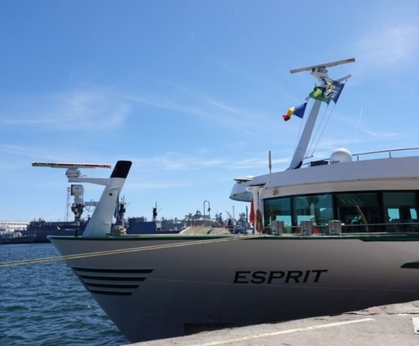 A luxury motor Yacht named Esprit moored at a marina with blue sky and flags on the mast.