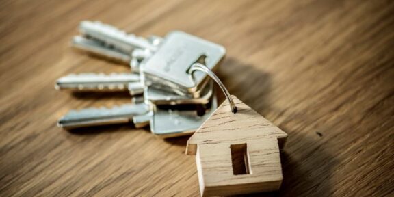 Keys on a keyring with a small wooden house tag, placed on a wood surface, symbolizing home ownership or real estate access.
