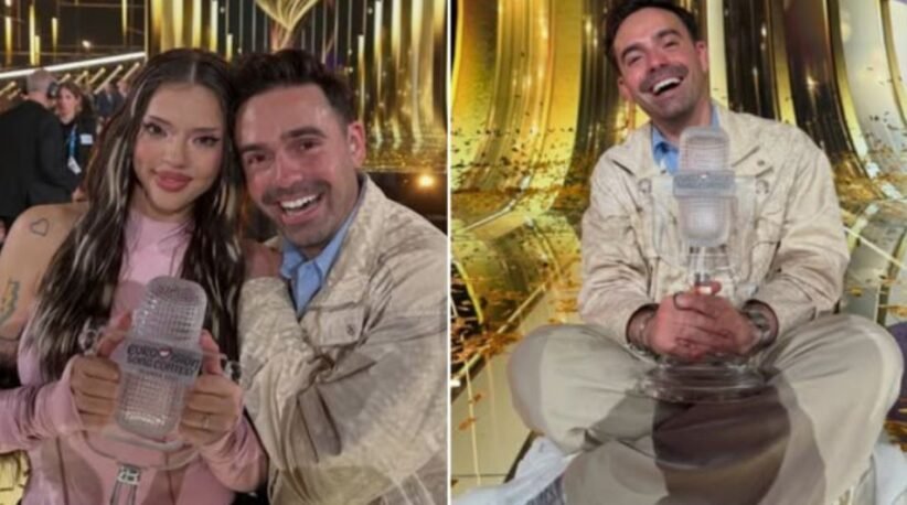Woman in pink holds a clear Eurovision trophy while a smiling man stands beside her in a glittering backstage area.