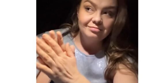 Woman with long hair smiling while clapping her hands, wearing a light blue top.