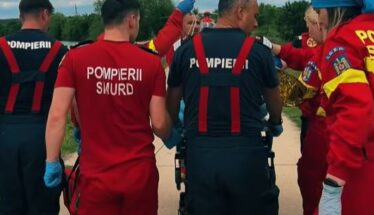 Emergency responders in red and dark uniforms gather around a patient on a wheeled stretcher outdoors during a rescue.