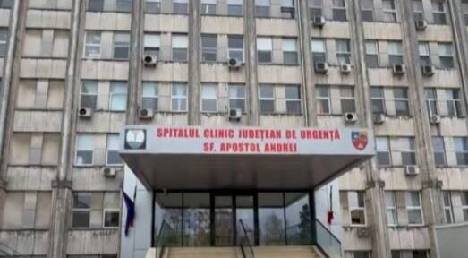 Front entrance of a large hospital building with stairs and glass doors, sign reads 'Spitalul Clinic Judetean de Urgenta Sf. Apostol Andrei'