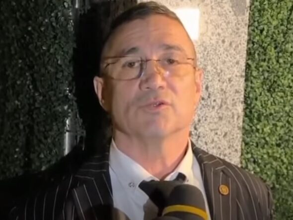 Man in a pinstripe suit being interviewed, speaking into a microphone.