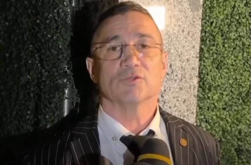 Man in a pinstripe suit being interviewed, speaking into a microphone.