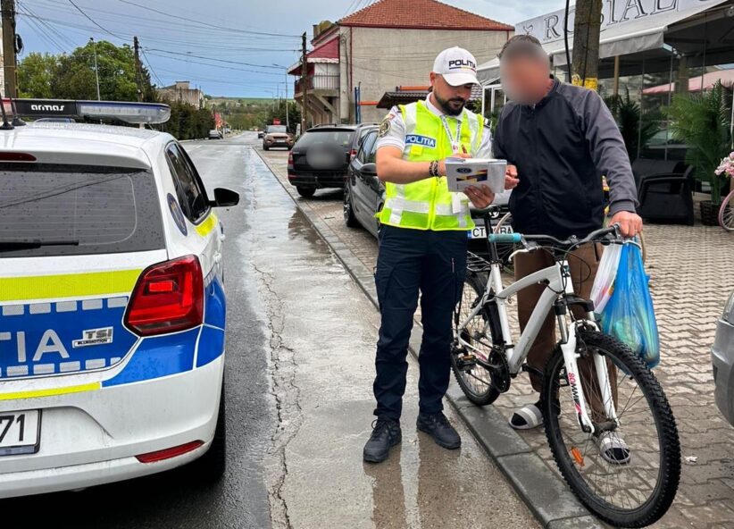 Police officer in a high-visibility vest analyzes a document with a man beside a white bike on a wet street by a police car.