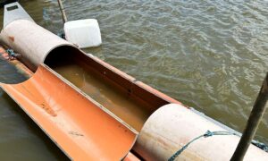 Orange buskin-like canoe split in half, floating in murky water with its hollow filled with water and tied ropes nearby.