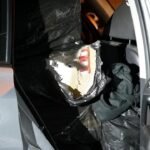 Open car door showing a large black plastic bundle inside the rear seat area of the car at night.