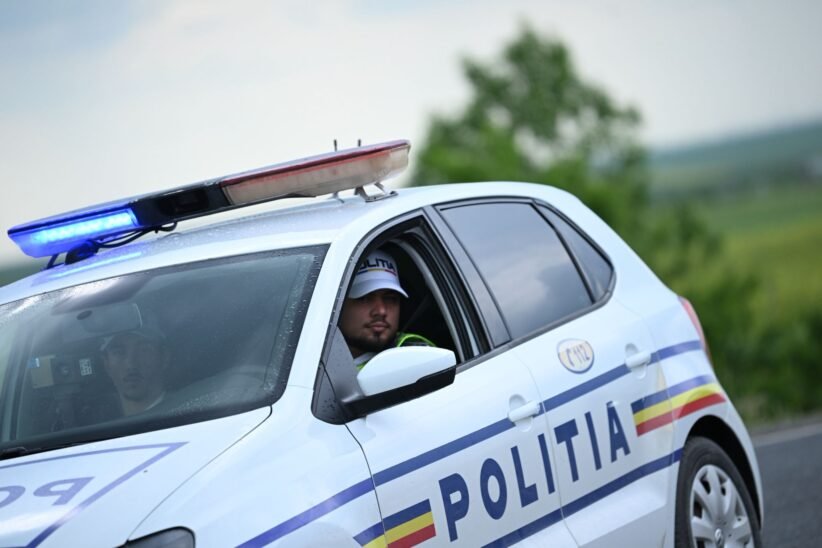 Romanian police car with blue emergency lights on; officer visible in the driver's seat.