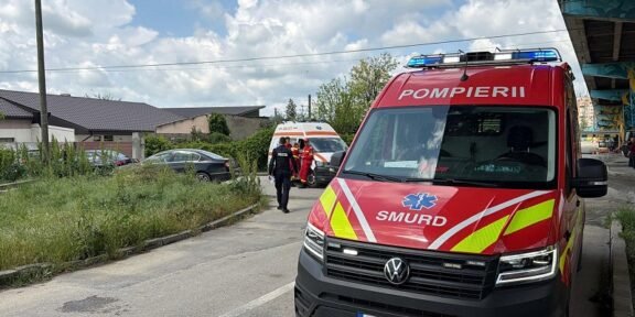 Red emergency ambulance with blue lights on the street, displaying SMURD and POMPIERII branding; rescue crew nearby.