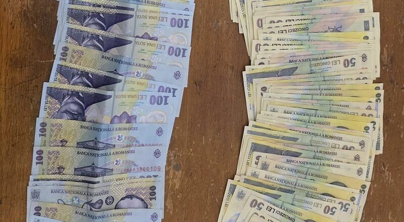 Two stacks of Romanian banknotes on a wooden table: blue 100-leu notes on the left and brownish 50-leu notes on the right.