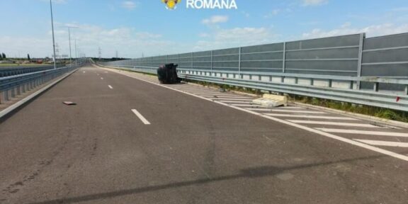 Wide highway scene with an overturned dark car on the right shoulder near the barrier; police logo reads 'Poliția Română'.