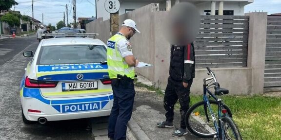 Policeman in a reflective vest writes on a clipboard beside a police car on a residential street.