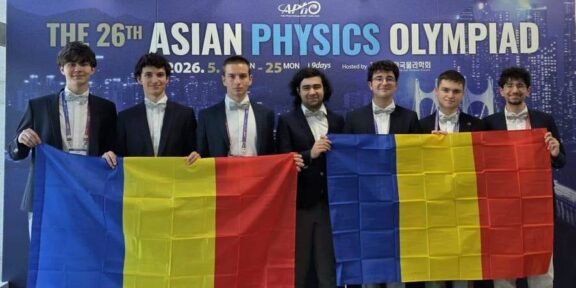 Seven young men in suits pose in front of a blue banner that reads 'The 26th Asian Physics Olympiad,' holding two Romanian flags with blue-yellow-red vertical stripes.