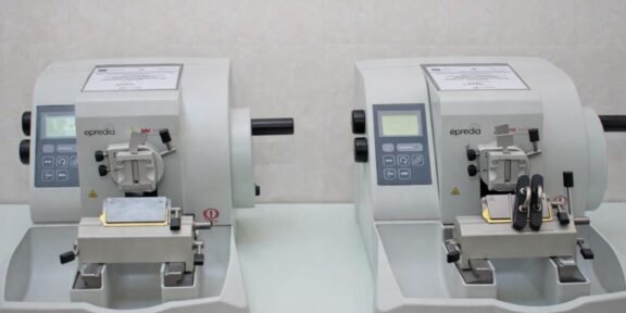 Two compact gray laboratory instruments with control panels sit side by side on a lab bench, each with a sample clamp and cutting area.