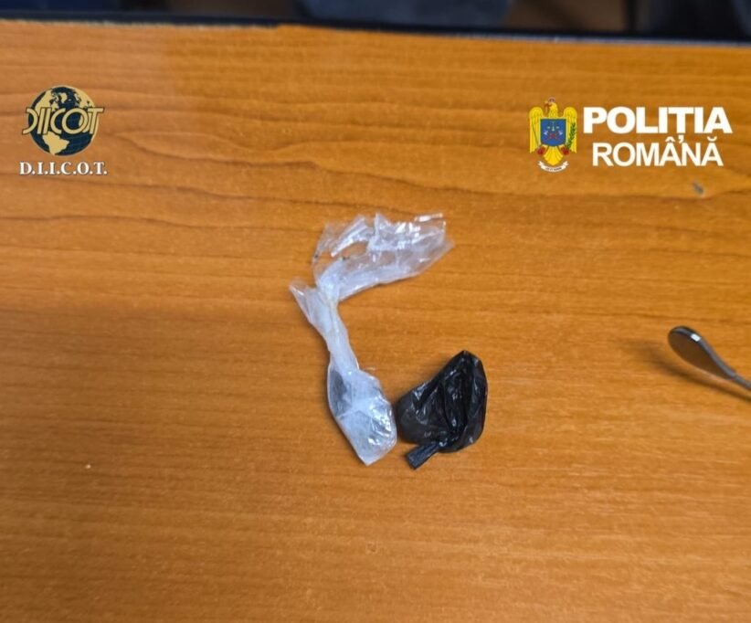 Two small plastic bags, one transparent and one black, lie on a wooden desk with police logos (Romania) in the corners, suggesting seized evidence.