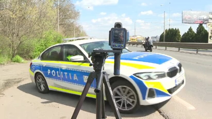 Romanian police car on a road with a speed camera mounted on a tripod in the foreground.