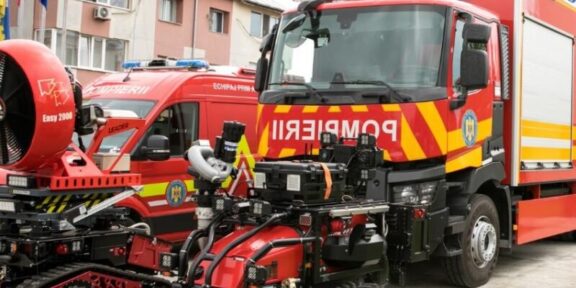 Red fire trucks with yellow chevrons parked in a lot, with a red tracked rescue robot in the foreground.