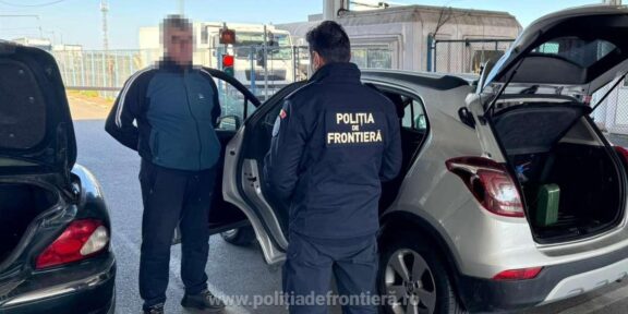 Border police officer in a dark uniform talks to a man at a car with the trunk open at a checkpoint. Frontière police patch visible on the jacket (text: POLIŢIA DE FRONTIERĂ).