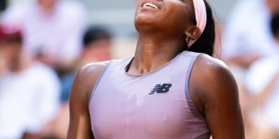 Athlete in a lavender sleeveless top and pink headband looks up with a smile as a crowd blurs in the background.