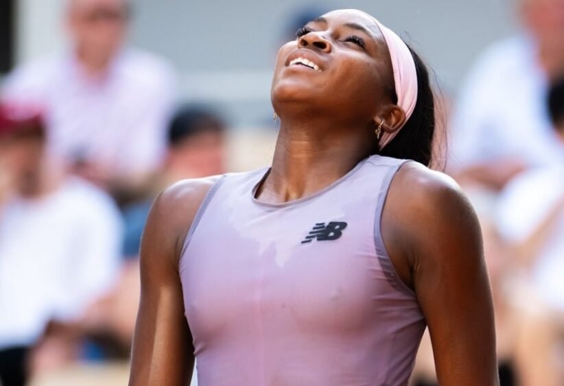 Athlete in a lavender sleeveless top and pink headband looks up with a smile as a crowd blurs in the background.
