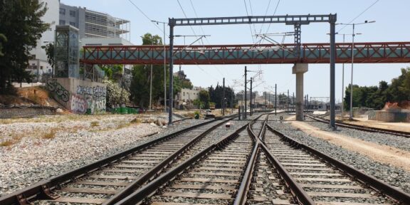 Railway tracks split and converge under overhead wires to the horizon, with graffiti walls on the left and a red bridge above.