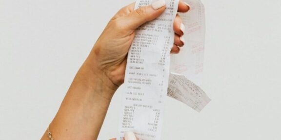 Hand holding a long, printed receipt strip between fingers with itemized text visible