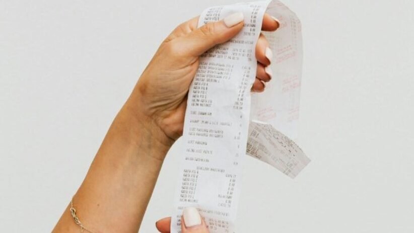 Hand holding a long, printed receipt strip between fingers with itemized text visible