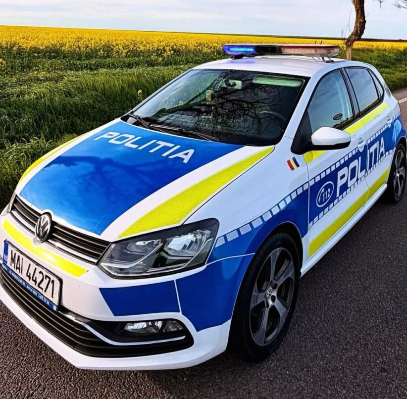 Politia police car in blue and white livery with blue and yellow stripes parked on a rural road by a yellow-field, front angled toward viewer (Romanian police).