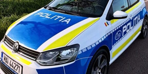 Politia police car in blue and white livery with blue and yellow stripes parked on a rural road by a yellow-field, front angled toward viewer (Romanian police).