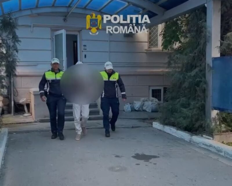 Two Romanian police officers escort a detainee with face blurred outside a building marked Politia Romana.