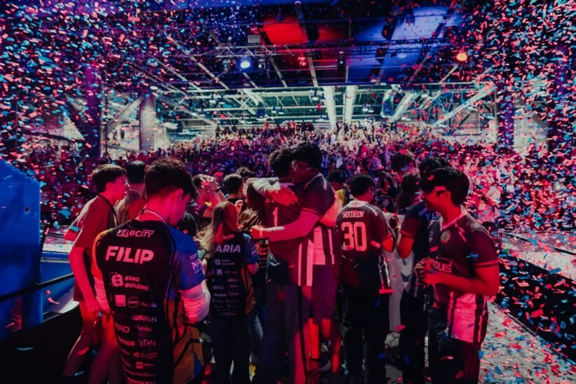 Crowded esports arena celebrating on stage with colorful confetti showering over players and fans.