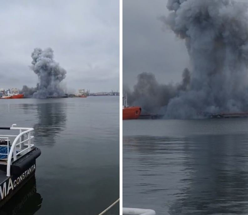 Port scene with a tall, dark smoke plume rising from a fire on the water, several ships in the distance and calm, overcast water nearby.