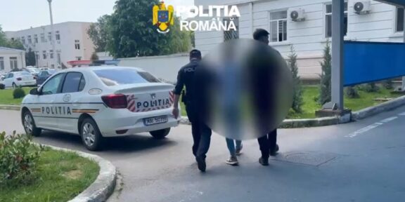 Romanian police car parked outside a building as officers escort two blurred individuals into the entrance.